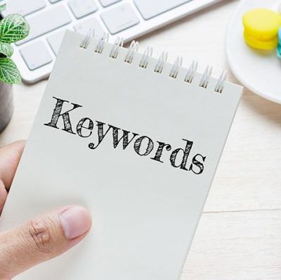 Hand holding a piece of paper with the word 'Keyword' written on it, symbolizing keyword research in SEO